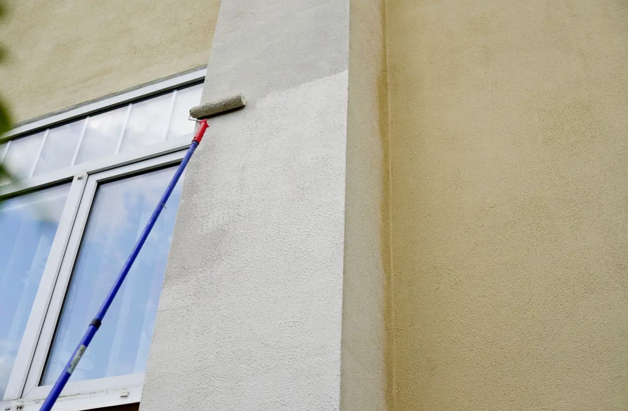Long-handled roller applying paint to an exterior stucco wall