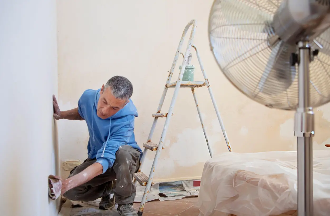 Painter kneeling to prep a wall inside an HOA community unit