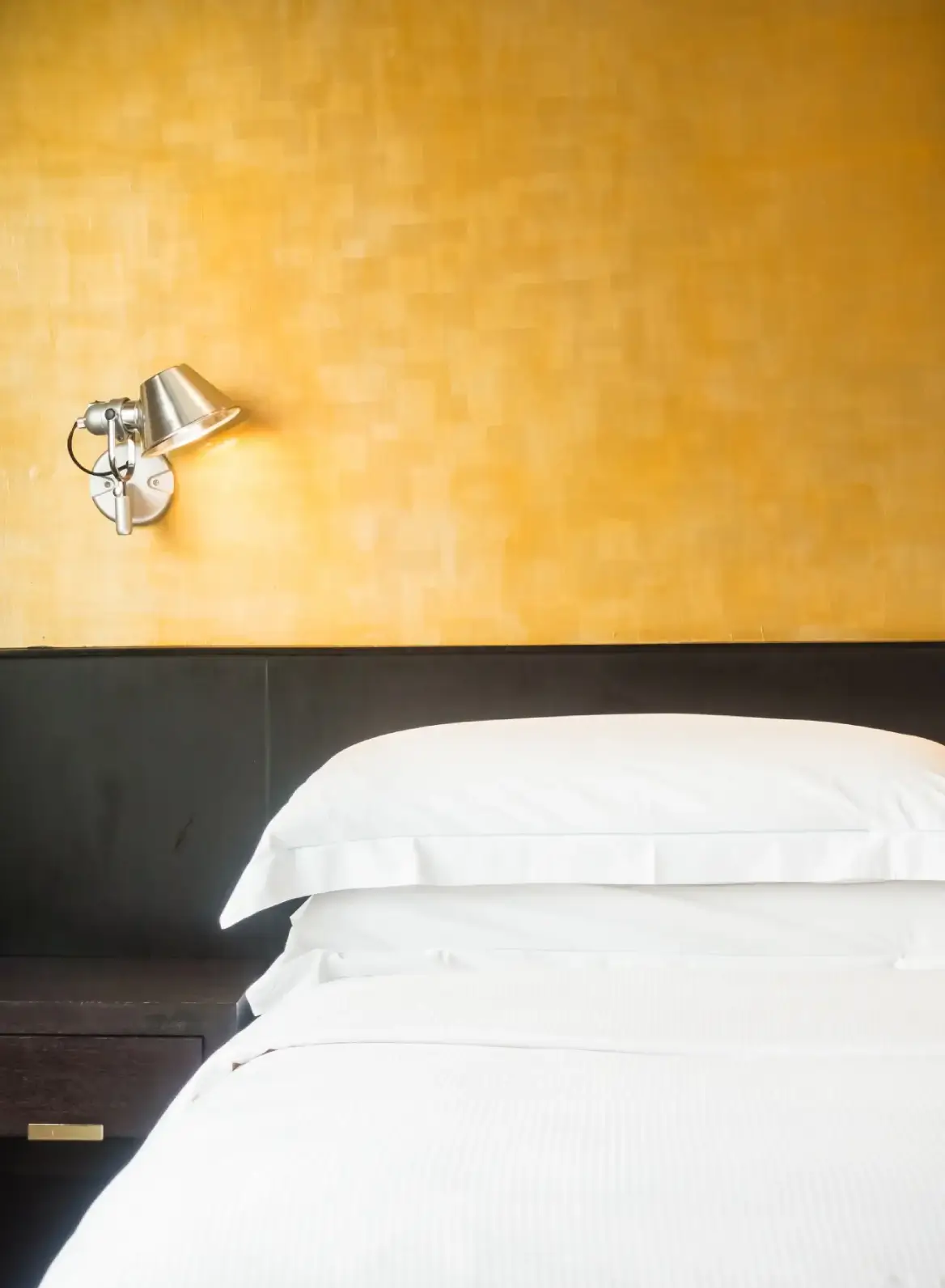 Bedroom wall painted in a warm gold tone beside white bedding