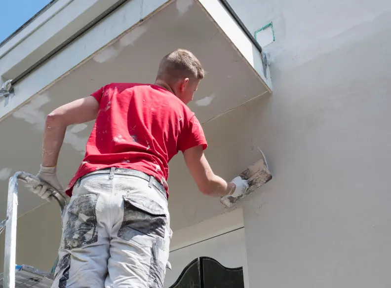 Painter in a red shirt painting an exterior eave from a ladder