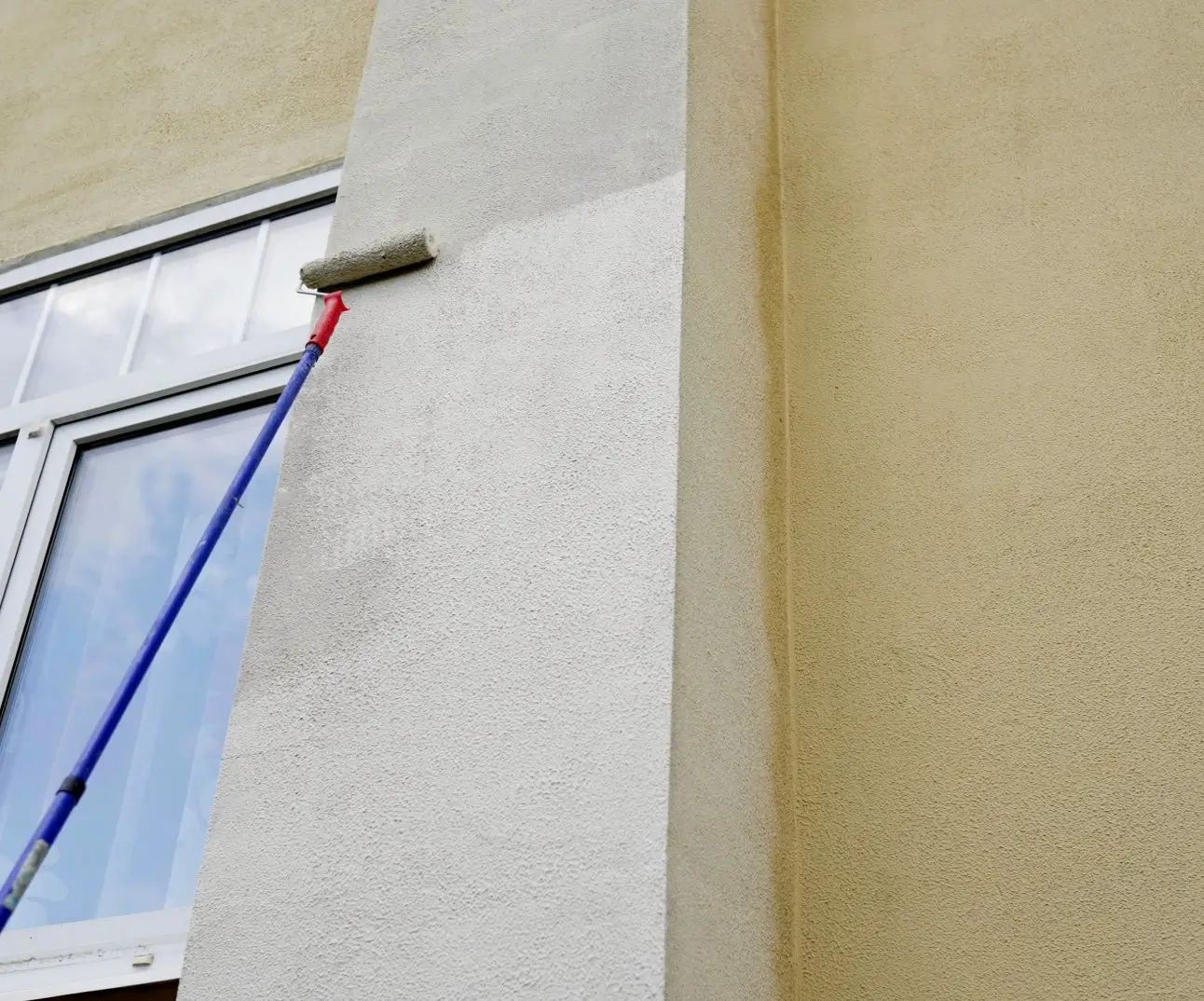 Painter applying fresh exterior paint to a coastal property wall