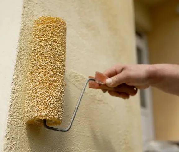 Hand rolling paint onto a wall with a roller brush